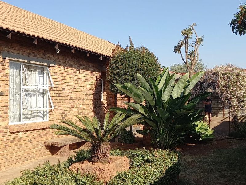 A rear view of the house featuring a face brick exterior, tiled roof, and established garden with a stone bench.
