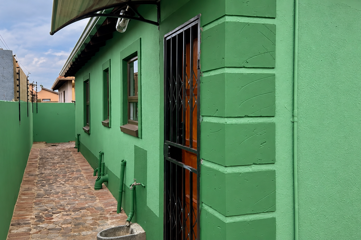 A side exterior view of the property featuring a stone paved walkway, security gate, and electric fencing along the boundary wall.