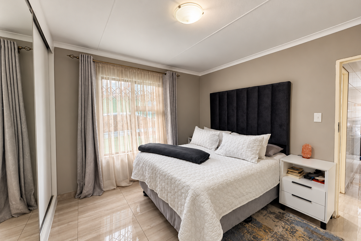 A well-maintained bedroom featuring tiled flooring, a built-in mirrored wardrobe, and a window fitted with security bars.