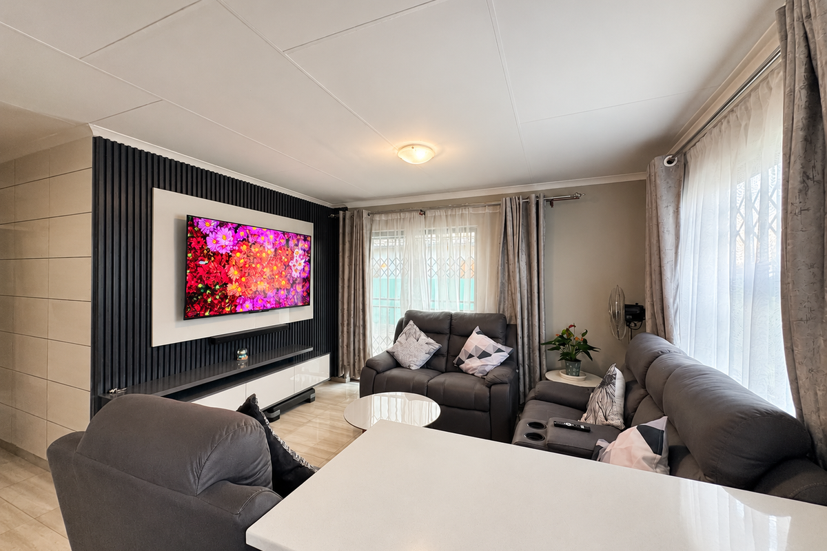 A modern living room featuring a contemporary slatted feature wall, tiled flooring, and large windows with security gates, offering a bright and well-maintained space.