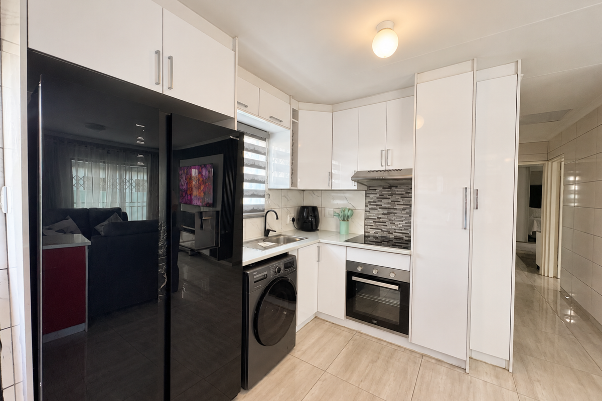 Modern kitchen featuring white high-gloss cabinetry, integrated oven, extractor fan, and tiled backsplash, seamlessly connected to the living area.