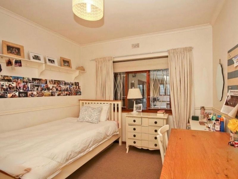 A cozy bedroom featuring carpet flooring, built-in shelving, and a window fitted with security bars.