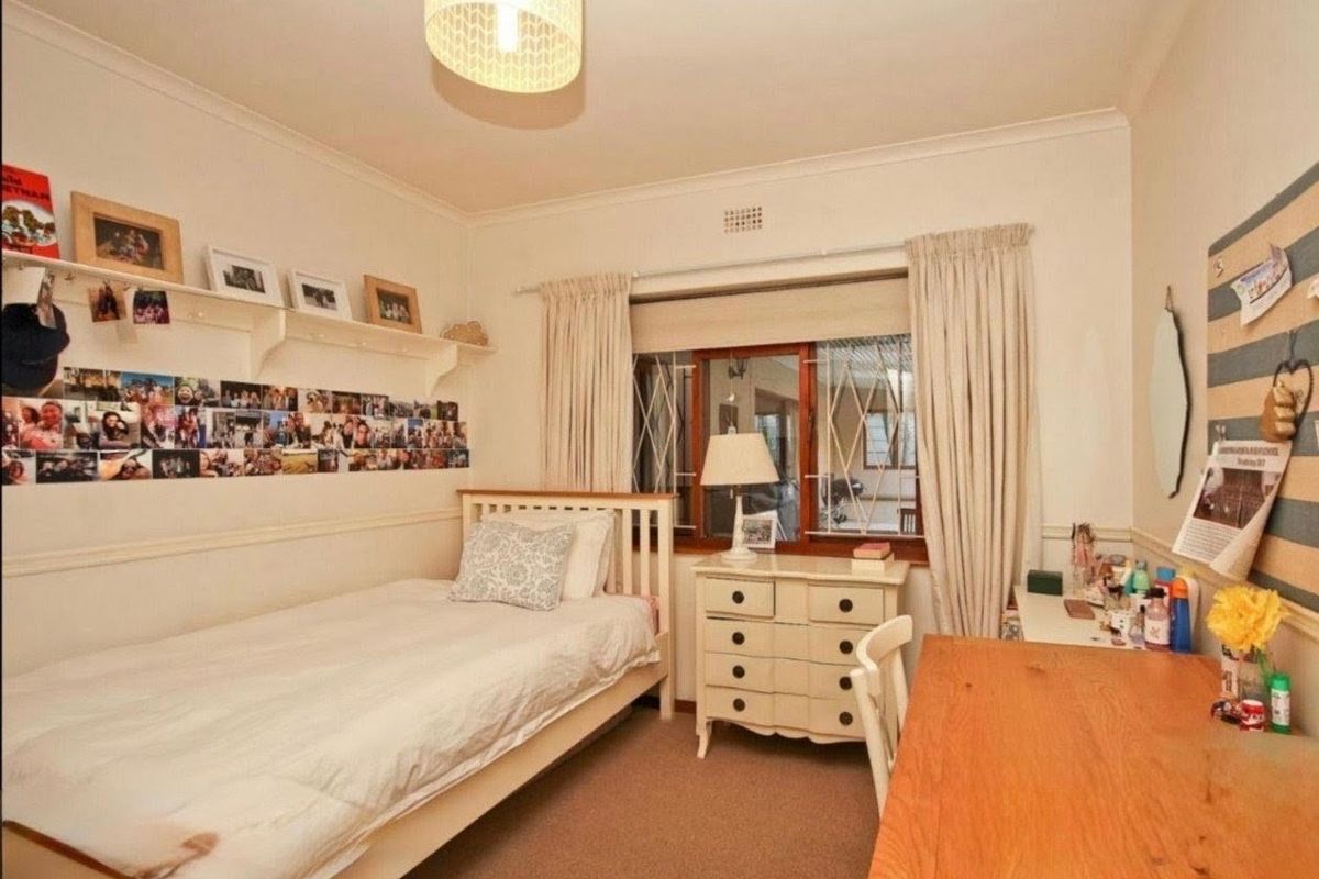 A cozy bedroom featuring carpet flooring, built-in shelving, and a window fitted with security bars.