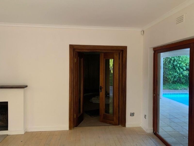 Spacious living area featuring timber flooring, a fireplace, and double timber doors leading to an outdoor patio and pool area.