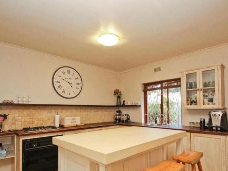 A functional kitchen featuring built-in cabinetry, a central island, tiled backsplash, and integrated oven and hob, with direct access to the garden.