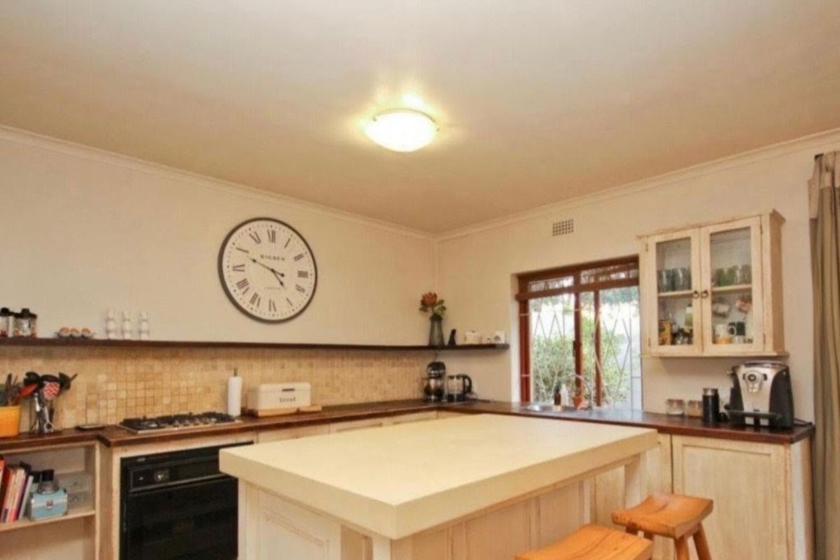 A functional kitchen featuring built-in cabinetry, a central island, tiled backsplash, and integrated oven and hob, with direct access to the garden.