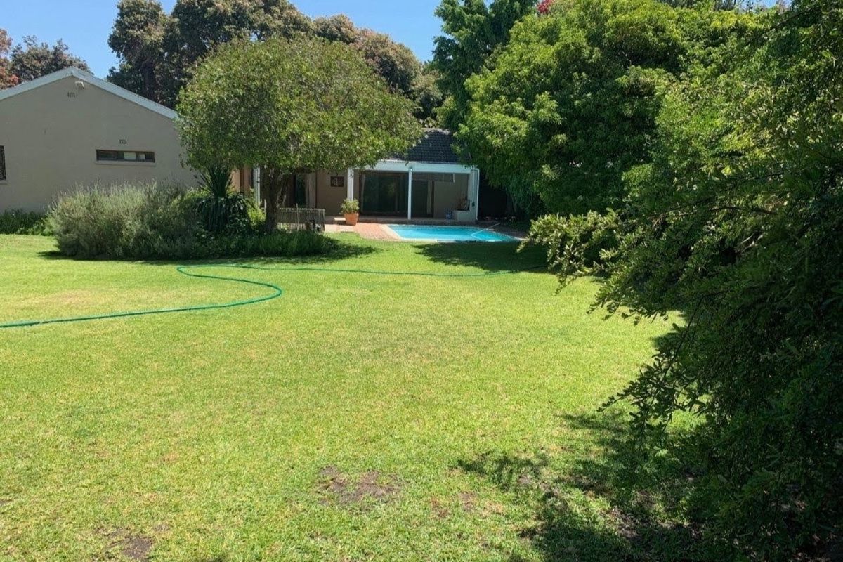 Spacious rear garden featuring a well-maintained lawn, mature trees, and a swimming pool with an adjacent covered patio area.