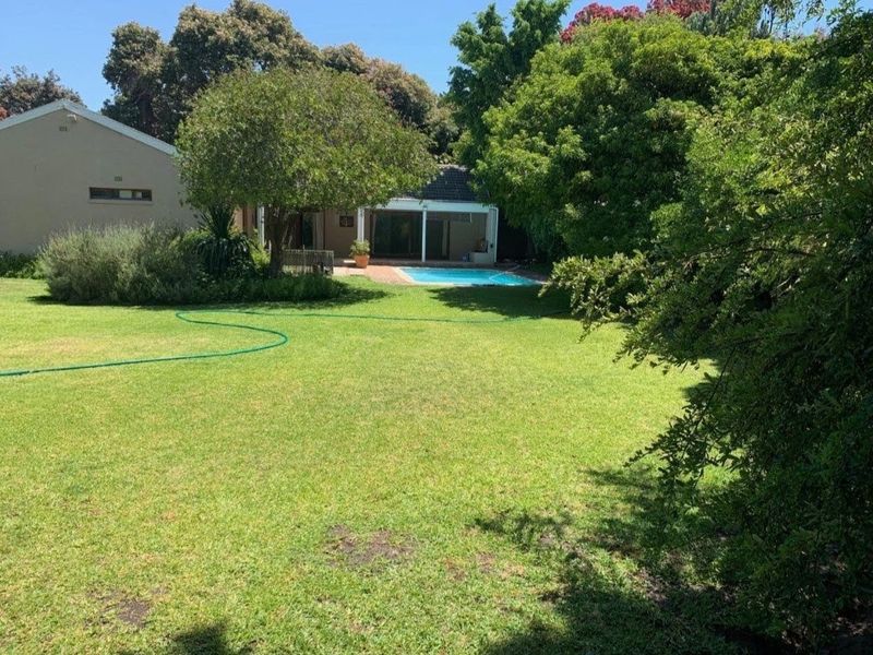 Spacious rear garden featuring a well-maintained lawn, mature trees, and a swimming pool with an adjacent covered patio area.