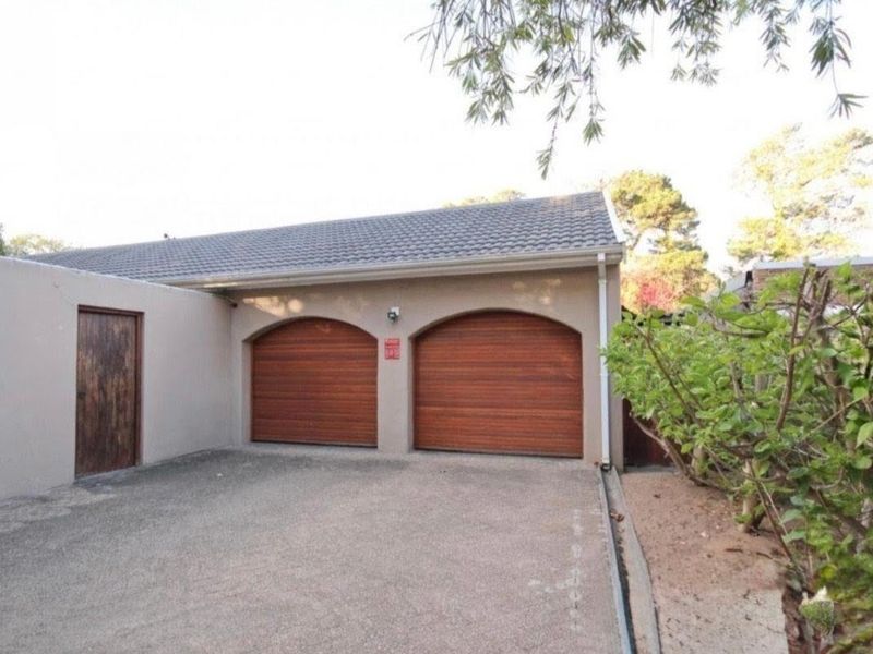 A double garage featuring arched wooden doors, a concrete driveway, and a side access door, set within a well-maintained exterior area.