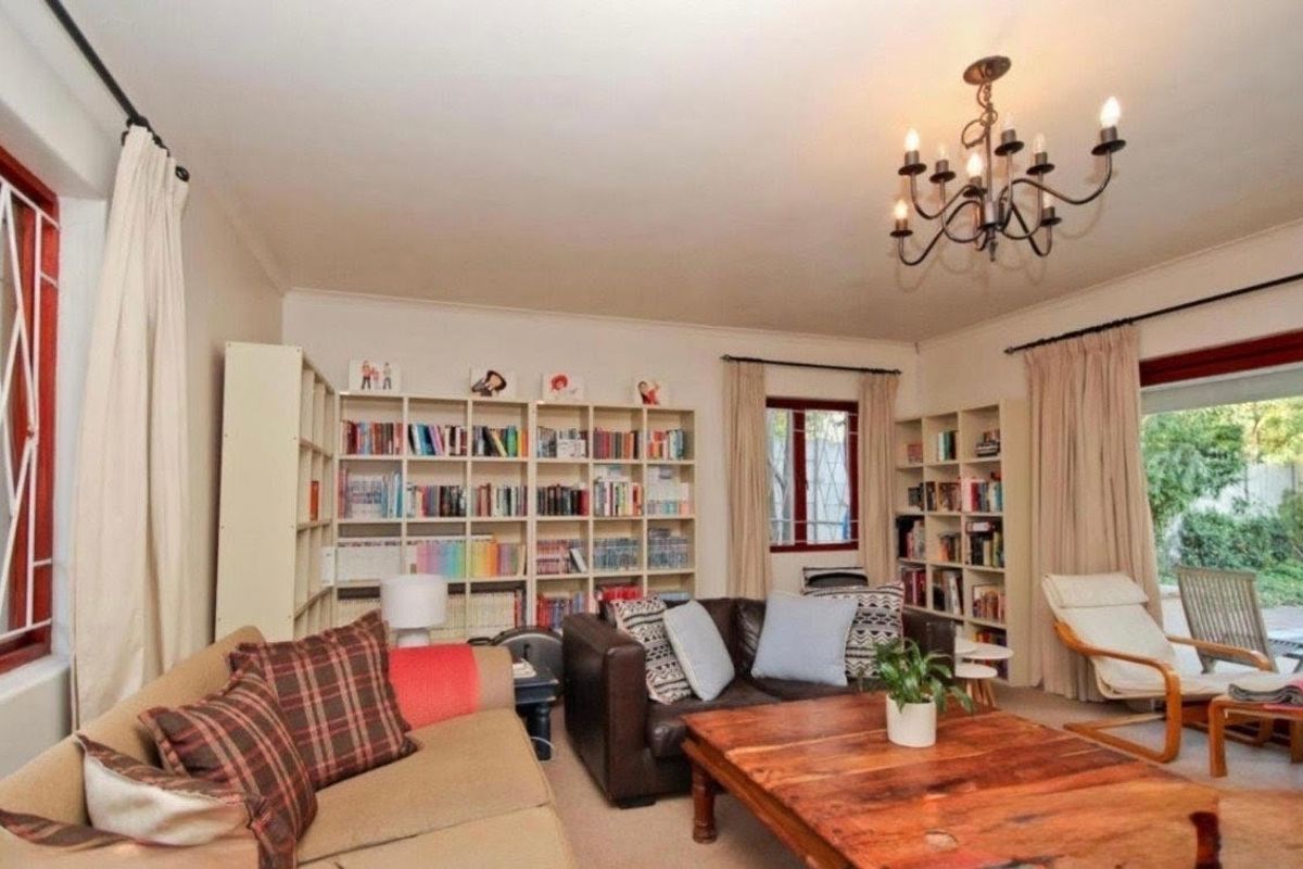 A comfortable living room featuring a classic chandelier, carpeted flooring, and large windows with burgundy frames, providing access to the outdoor area.