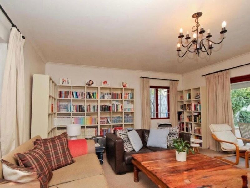 A comfortable living room featuring a classic chandelier, carpeted flooring, and large windows with burgundy frames, providing access to the outdoor area.