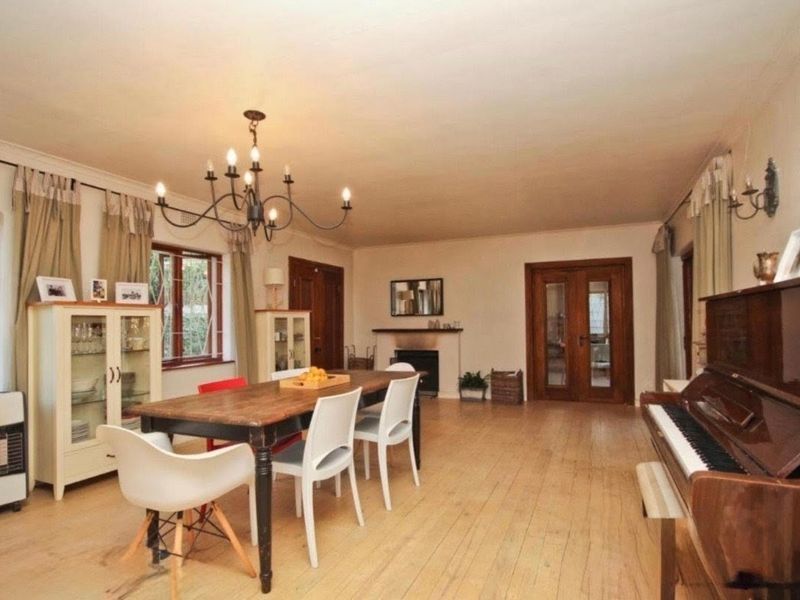 Spacious dining room featuring hardwood flooring, a classic fireplace, elegant chandelier lighting, and traditional wooden french doors leading to adjacent living spaces.