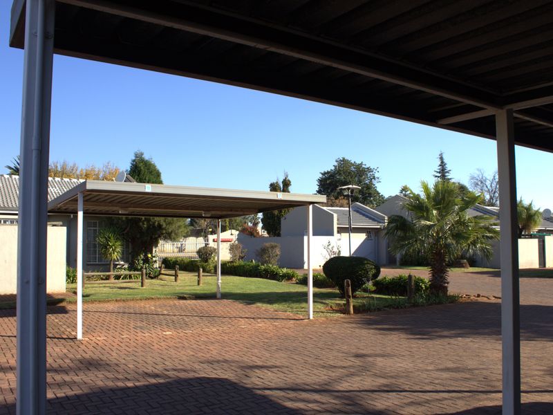 A covered carport area with paved driveway and surrounding landscaped garden within a residential cluster complex.