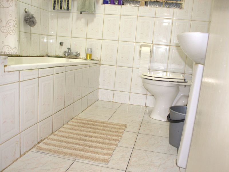 A dated bathroom featuring a built-in bathtub, pedestal basin, and toilet with original ceramic wall and floor tiling.