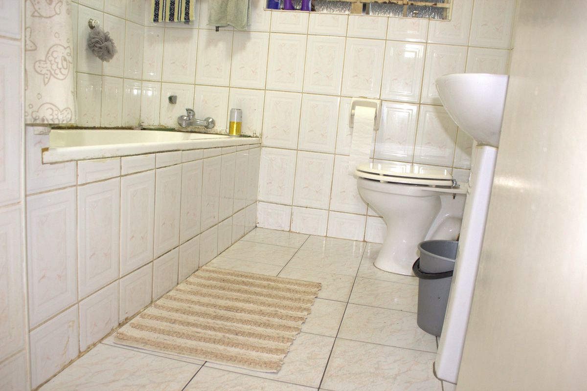 A dated bathroom featuring a built-in bathtub, pedestal basin, and toilet with original ceramic wall and floor tiling.
