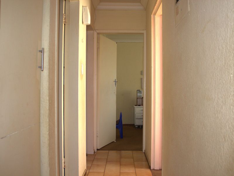 A narrow residential hallway with tiled flooring and multiple internal doorways, showing signs of wear and requiring cosmetic updates.