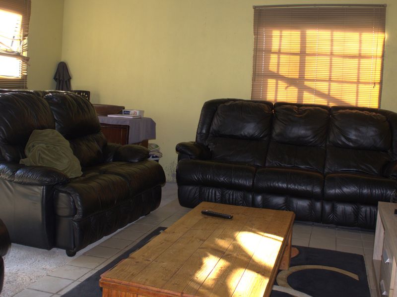 A living room featuring tiled flooring and venetian blinds, currently showing signs of wear on the walls.