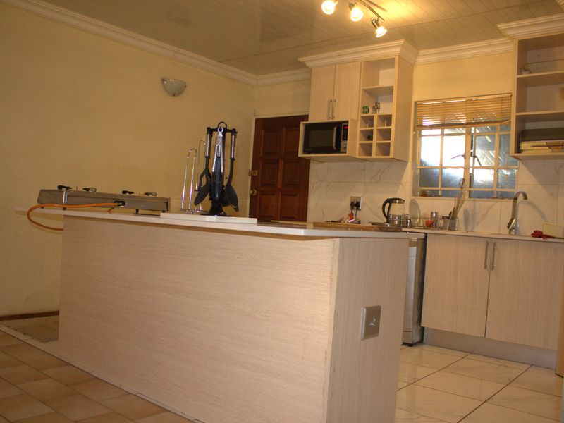 A functional kitchen featuring light wood-finish cabinetry, a central island, tiled flooring, and built-in microwave, offering a practical layout for daily meal preparation.