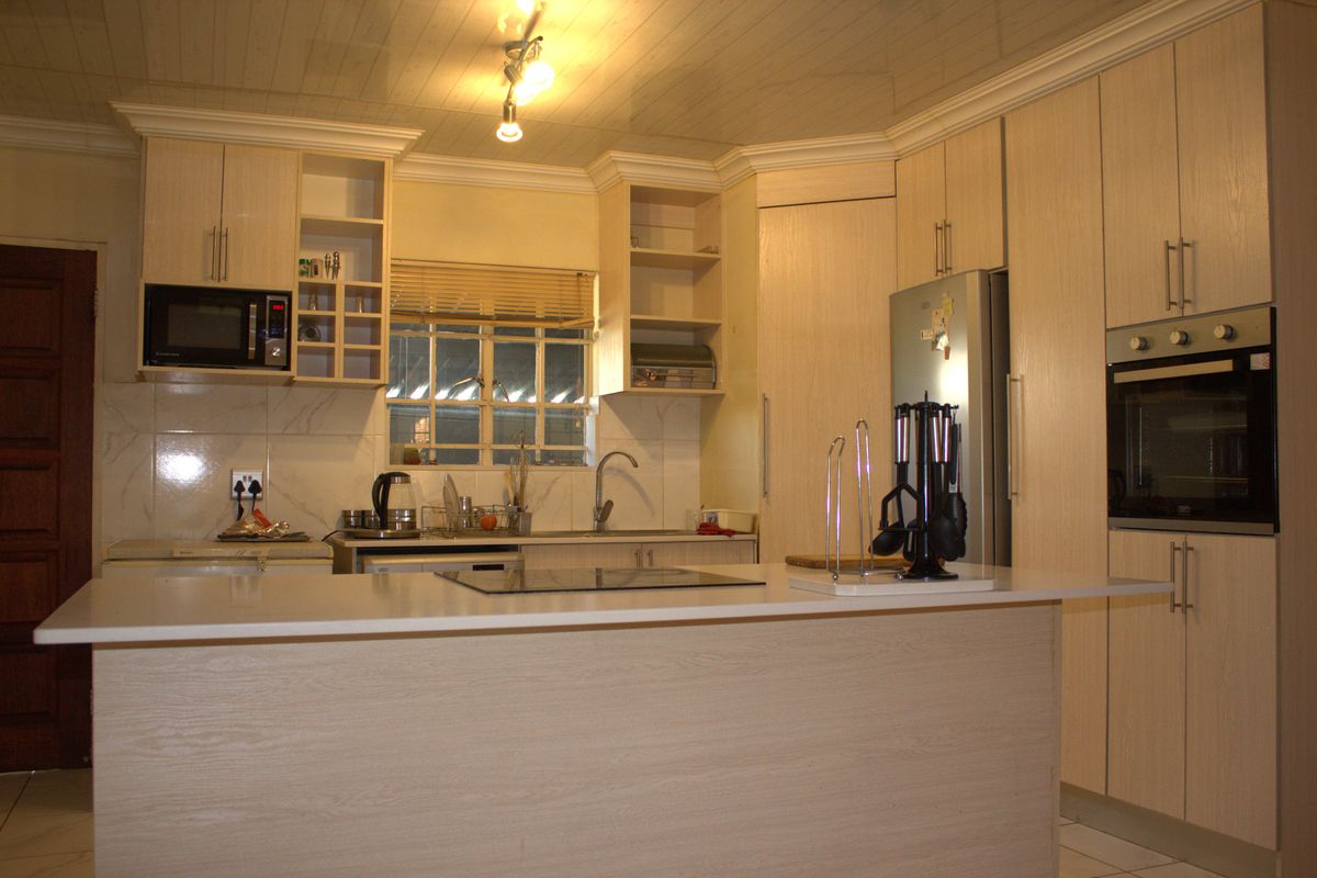A functional kitchen featuring light wood-grain cabinetry, a central island with a hob, built-in oven, microwave, and tiled backsplash with a double sink.