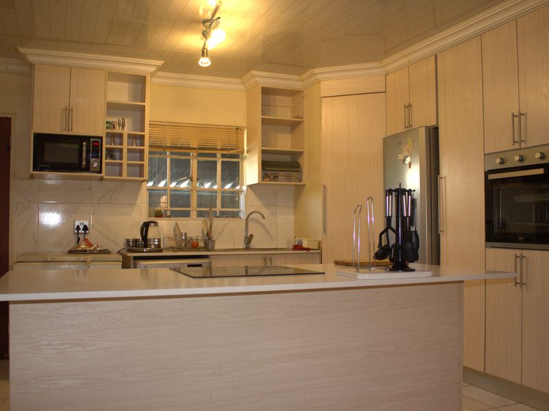 A functional kitchen featuring light wood-grain cabinetry, a central island with a hob, built-in oven, microwave, and tiled backsplash with a double sink.