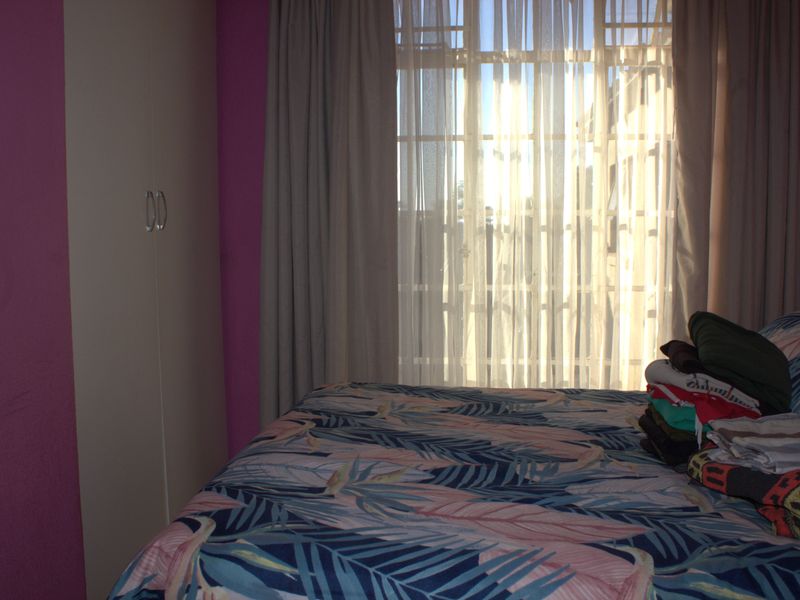 A bedroom featuring a built-in wardrobe and a window with security bars, allowing natural light into the space.