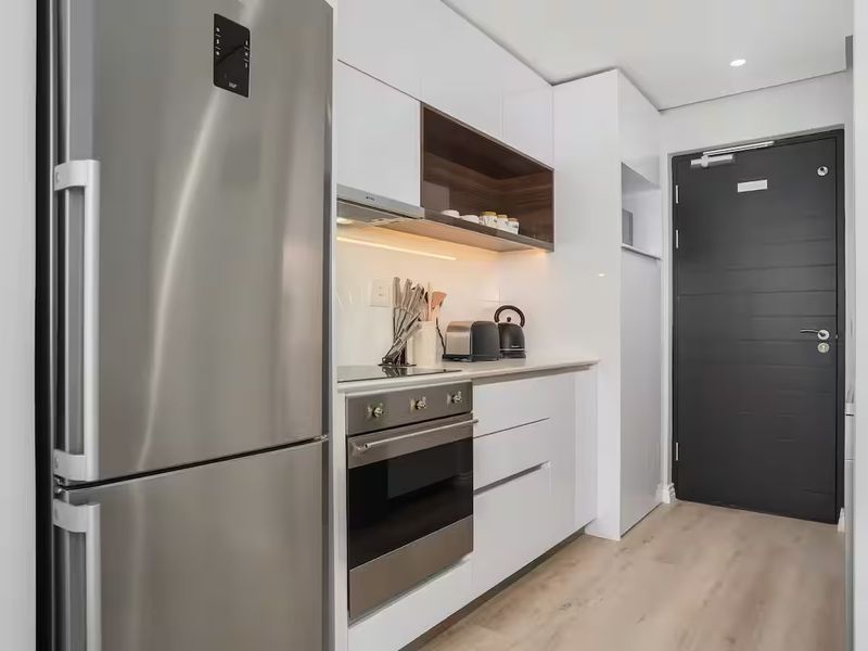 Modern kitchen featuring high-gloss white cabinetry, integrated stainless steel appliances, under-cabinet lighting, and durable laminate flooring in a clean, contemporary layout.