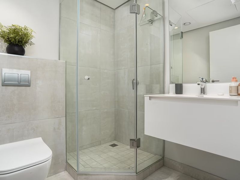 Modern bathroom featuring a wall-hung toilet with concealed cistern, a floating vanity, and a glass-enclosed shower with neutral tiling.