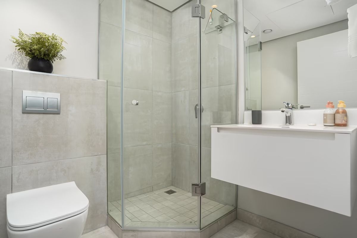 Modern bathroom featuring a wall-hung toilet with concealed cistern, a floating vanity, and a glass-enclosed shower with neutral tiling.