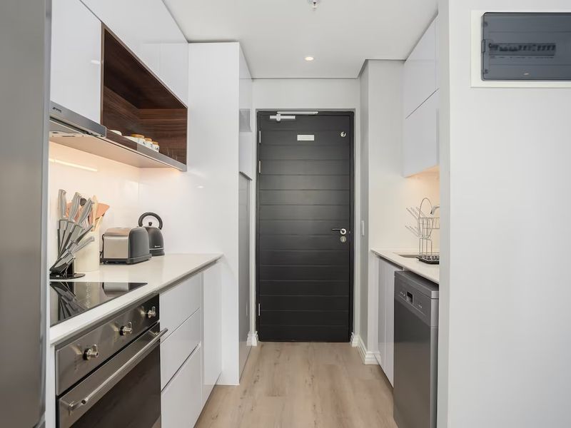 Modern galley-style kitchen featuring sleek white cabinetry, integrated appliances, electric hob, oven, and high-quality laminate flooring.