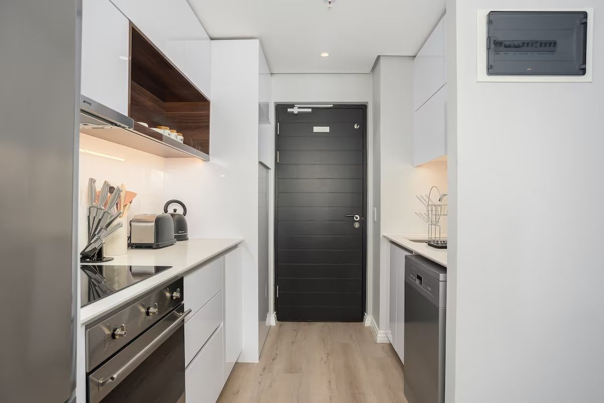 Modern galley-style kitchen featuring sleek white cabinetry, integrated appliances, electric hob, oven, and high-quality laminate flooring.