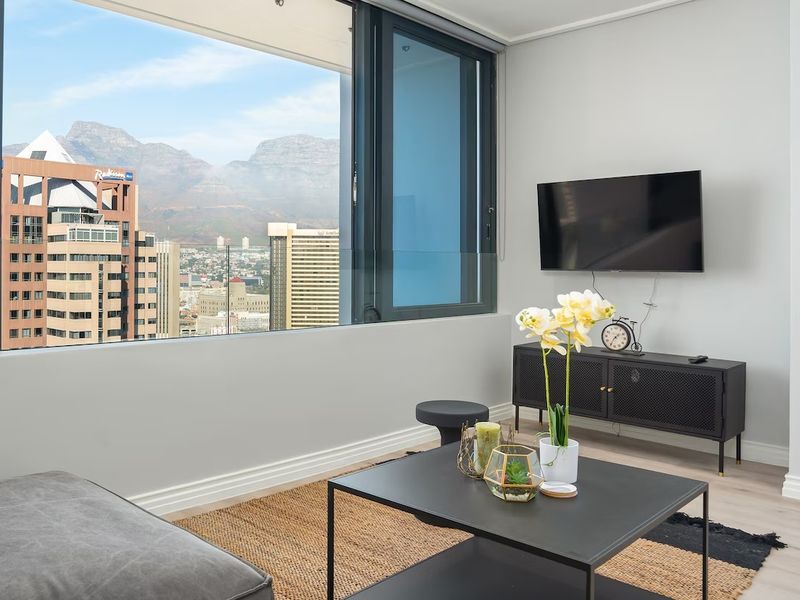 Modern living room featuring large floor-to-ceiling windows with expansive city and mountain views, complemented by sleek laminate flooring and neutral wall finishes.