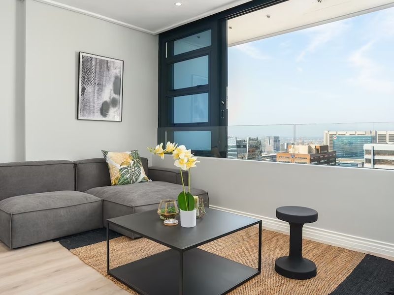 Modern living area featuring large windows with expansive city views, glass balustrade, recessed lighting, and high-quality laminate flooring.