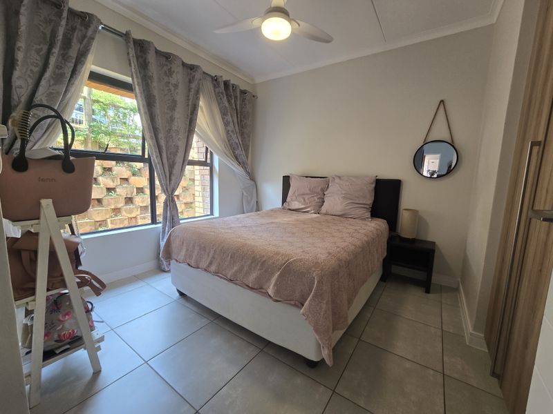 A well-lit bedroom featuring neutral tiled flooring, a ceiling fan, and a built-in wardrobe, offering a comfortable and functional living space.