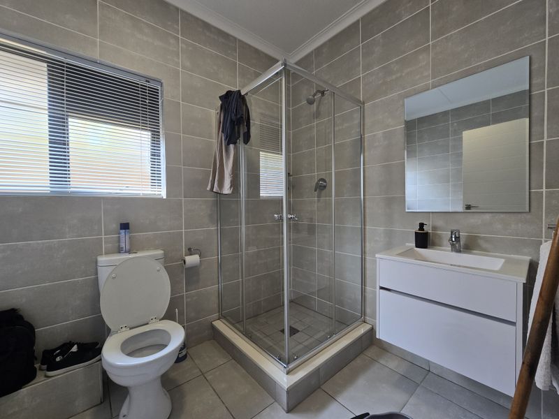 A modern bathroom featuring a glass shower enclosure, wall-mounted vanity with basin, and neutral floor-to-ceiling wall tiles.