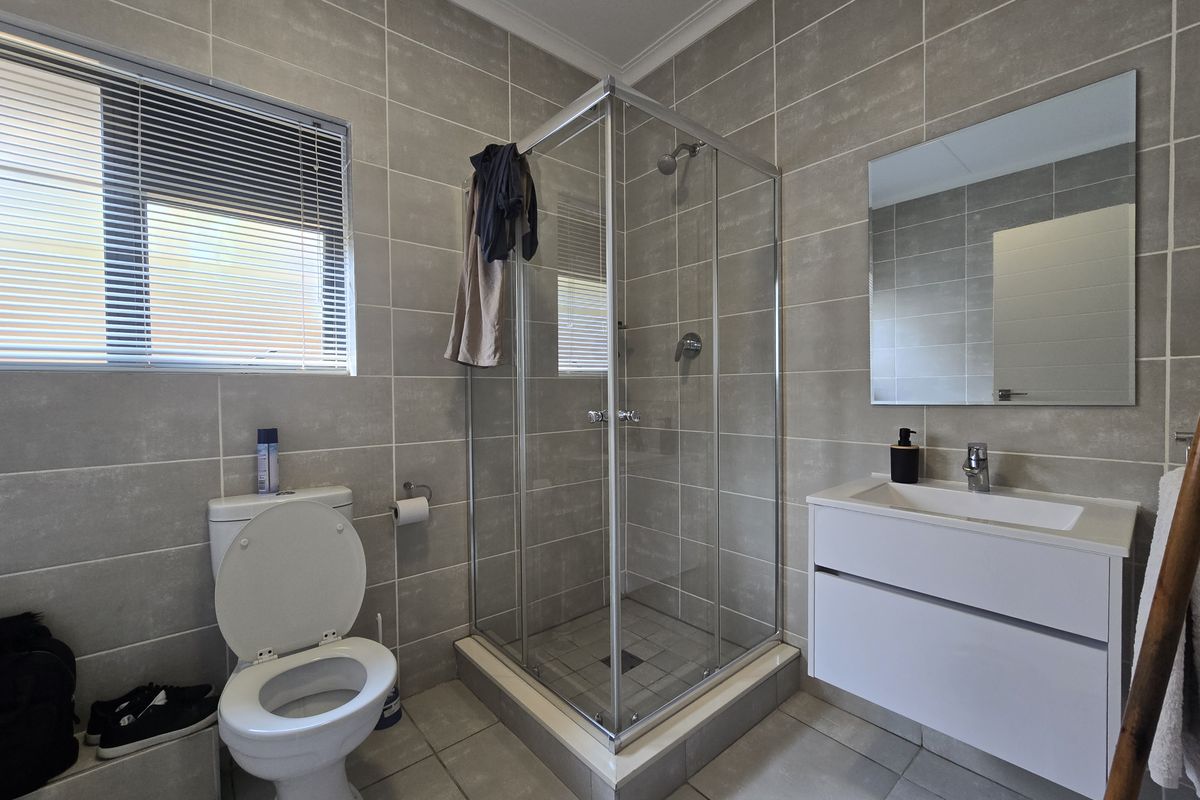 A modern bathroom featuring a glass shower enclosure, wall-mounted vanity with basin, and neutral floor-to-ceiling wall tiles.