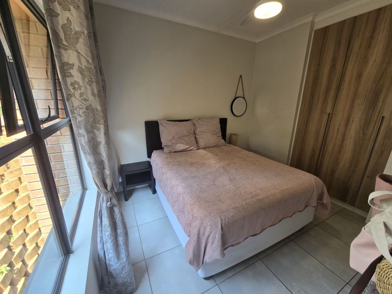 A well-maintained bedroom featuring tiled flooring, built-in wooden cupboards, and a large window providing natural light.