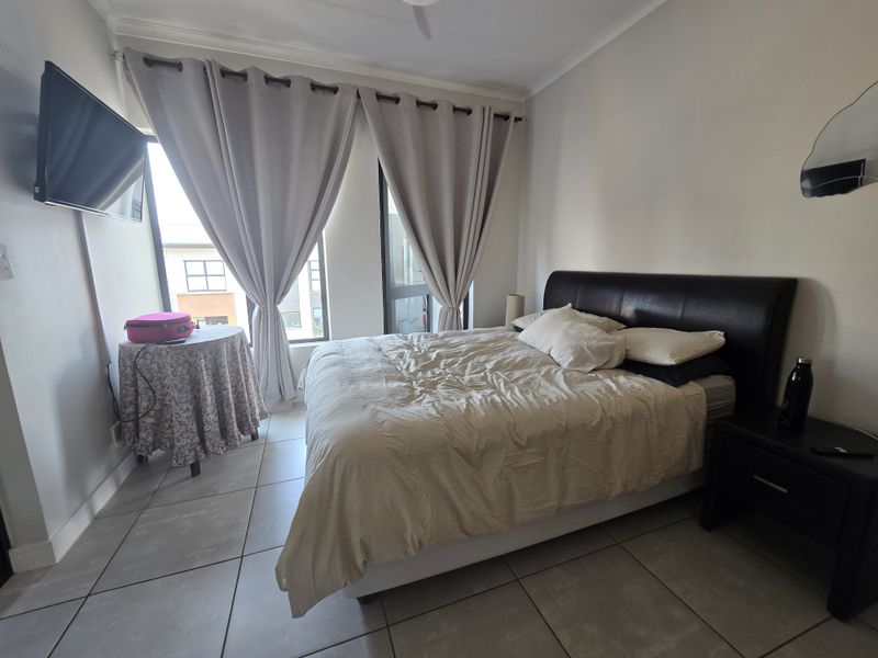 A functional bedroom featuring large windows, tiled flooring, and a ceiling fan, offering a neutral space ready for personalization.