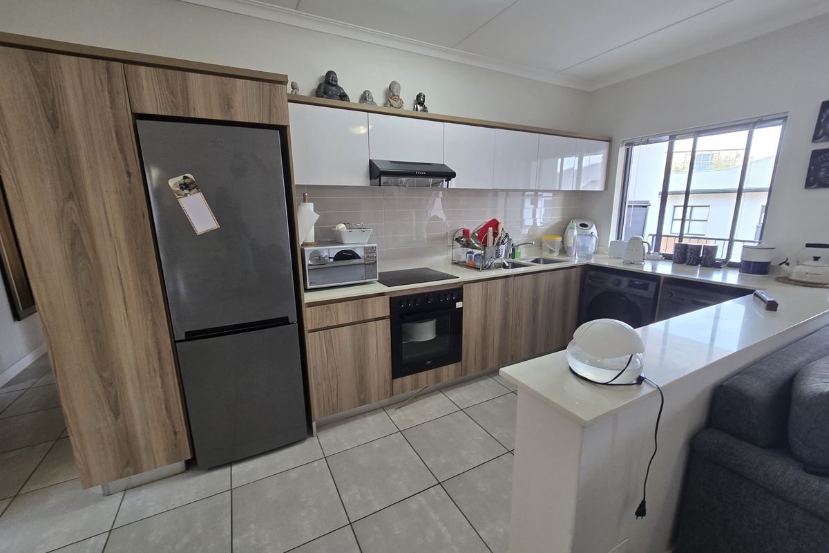 Modern kitchen featuring wood-grain cabinetry, white upper cabinets, integrated appliances, tiled backsplash, and a breakfast bar counter.