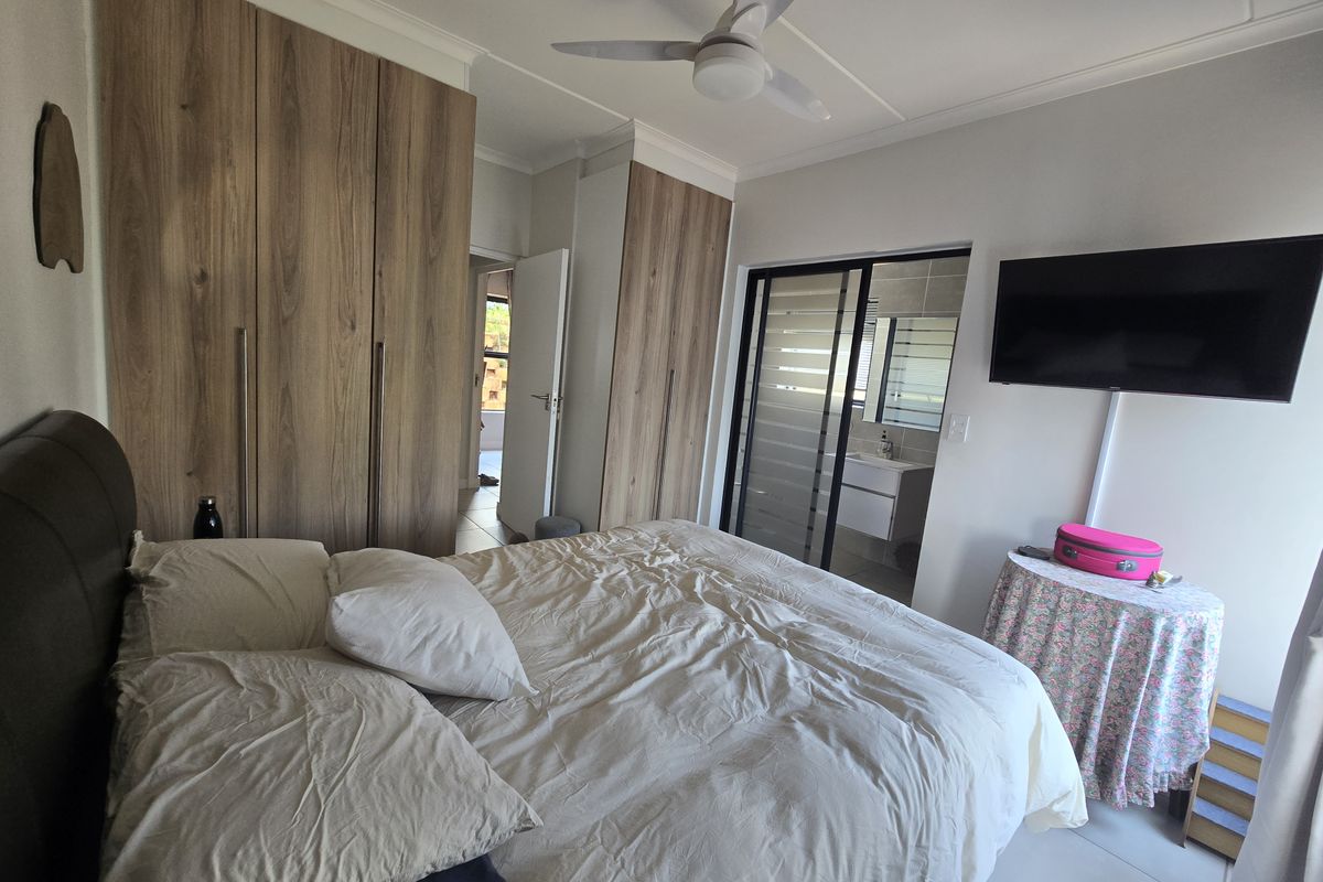 A well-maintained bedroom featuring extensive built-in wooden cupboards, a ceiling fan, and direct access to an en-suite bathroom with modern tiling.