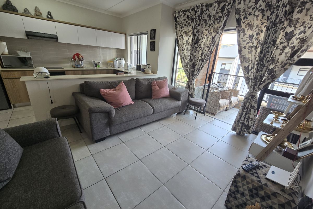 Open plan living area featuring a modern kitchen with built-in cabinetry and tiled flooring, leading directly to a private balcony through sliding glass doors.