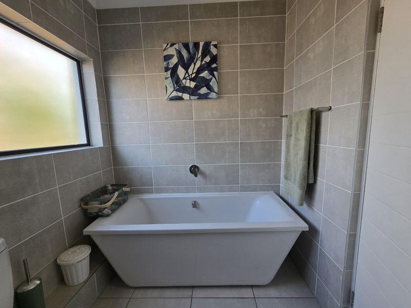 A modern bathroom featuring a clean freestanding bathtub, neutral ceramic wall and floor tiling, and a frosted glass window for privacy.