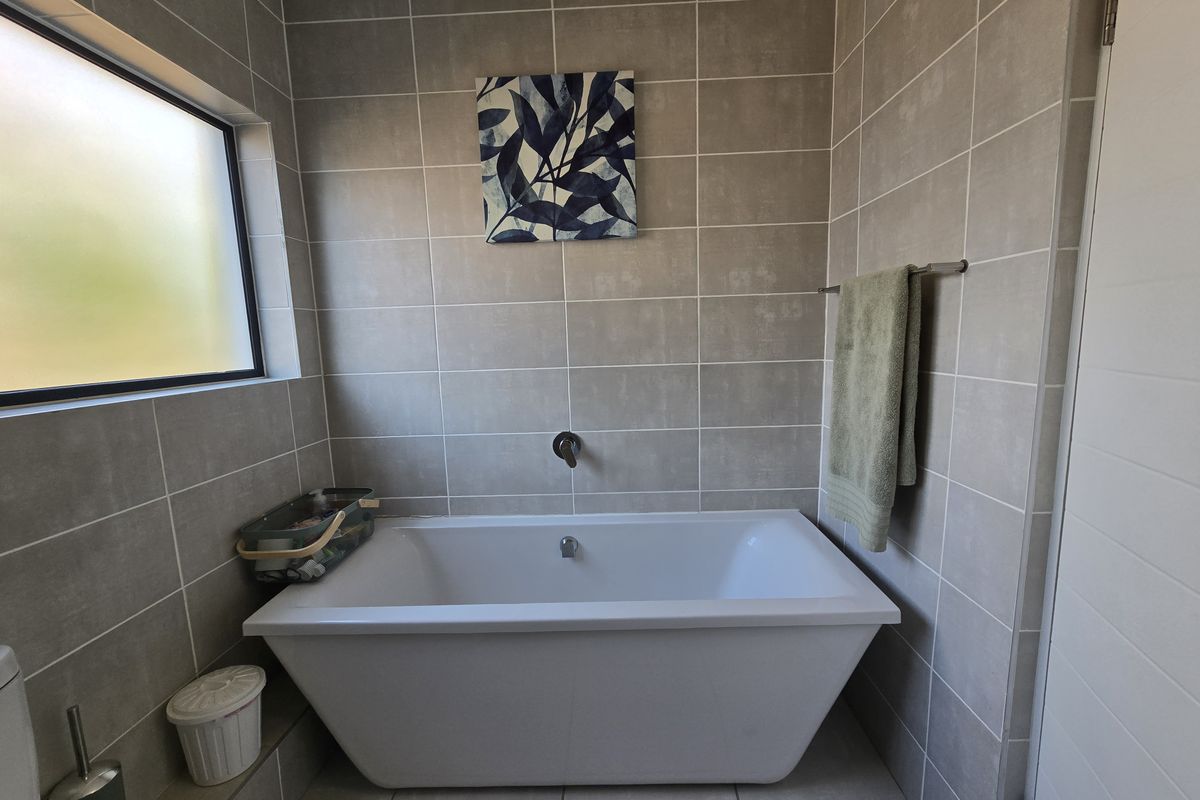 A modern bathroom featuring a clean freestanding bathtub, neutral ceramic wall and floor tiling, and a frosted glass window for privacy.