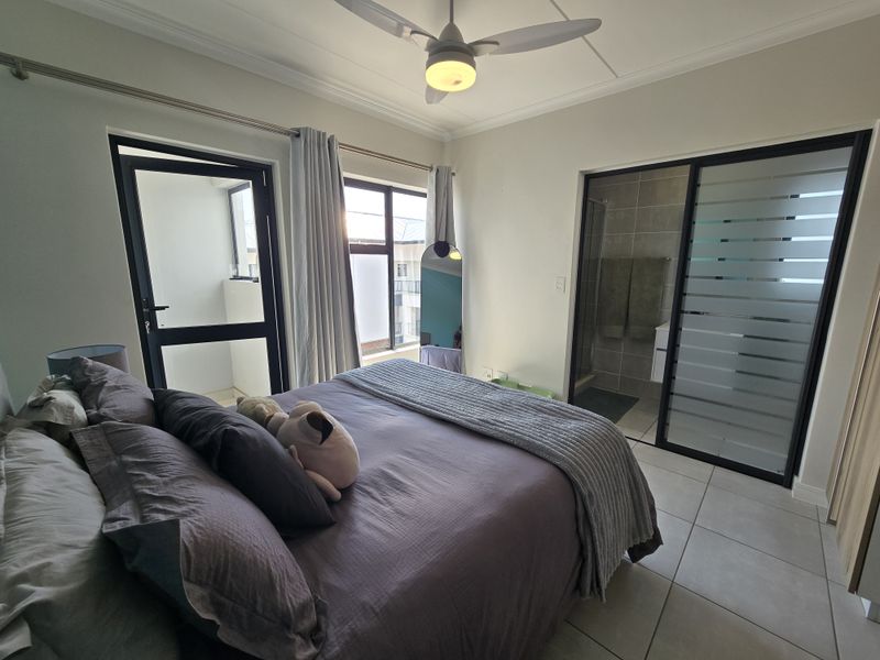 A well-maintained bedroom featuring tiled floors, a ceiling fan, an en-suite bathroom with a glass partition, and direct access to a private balcony.