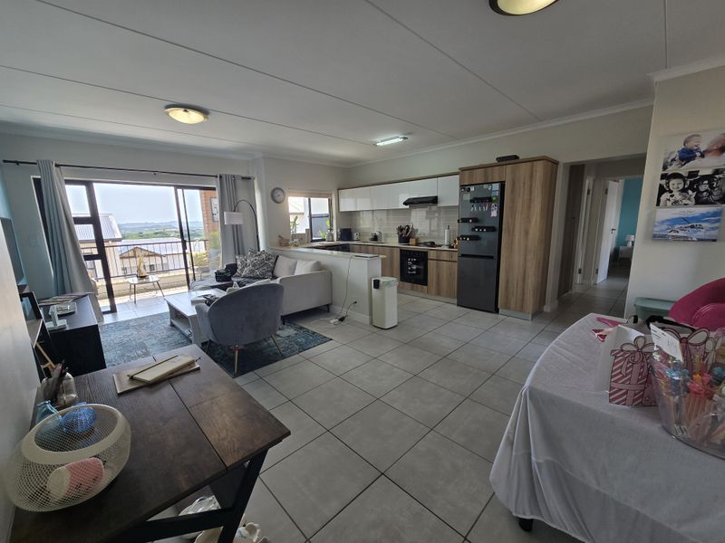 Spacious open-plan living area featuring a modern kitchen with built-in cabinetry, tiled floors, and seamless access to a private balcony with scenic views.