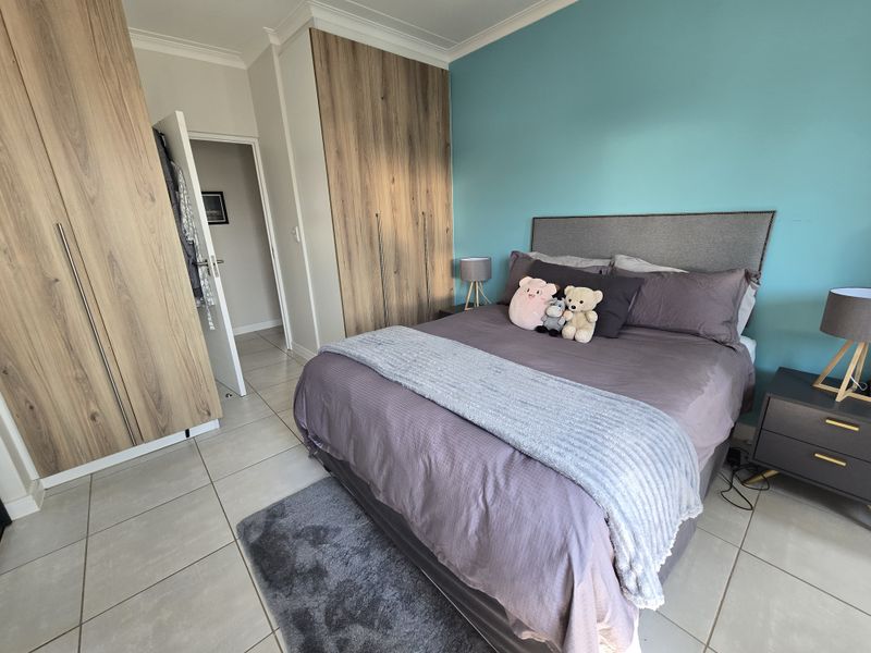 A well-maintained bedroom featuring modern wood-finish built-in cupboards, neutral tiled flooring, and a vibrant teal accent wall.