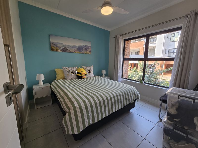 A well-lit bedroom featuring tiled flooring, a ceiling fan, and a large window with an accent wall.