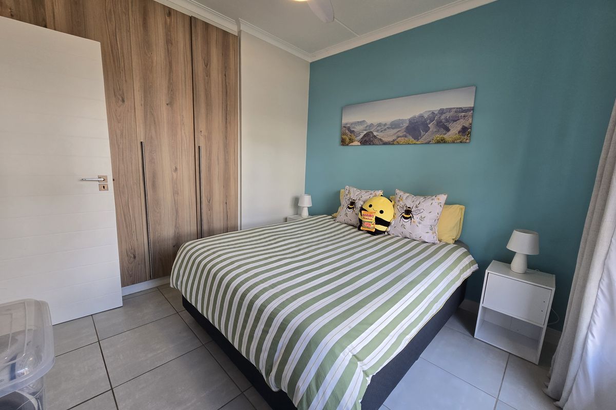 A well-maintained bedroom featuring built-in wooden cupboards, tiled flooring, and a ceiling fan, with a vibrant blue accent wall.