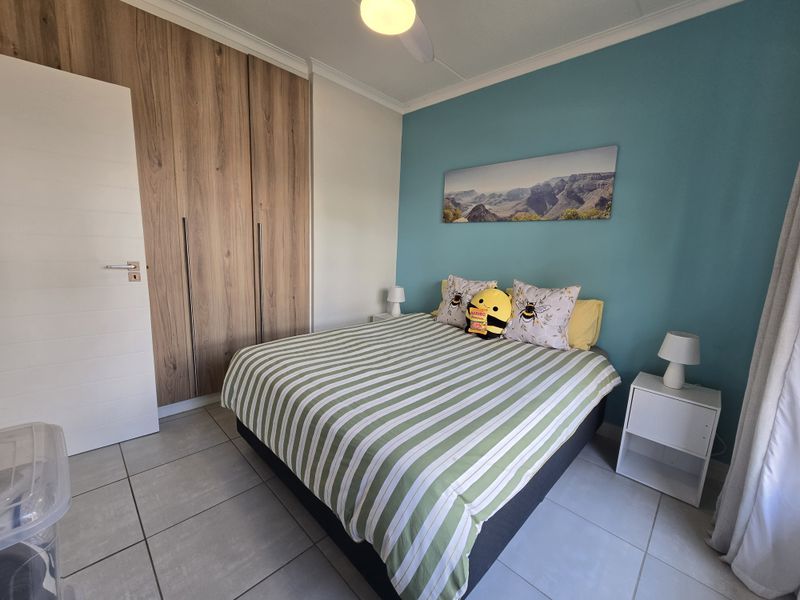 A well-maintained bedroom featuring built-in wooden cupboards, tiled flooring, and a ceiling fan, with a vibrant blue accent wall.