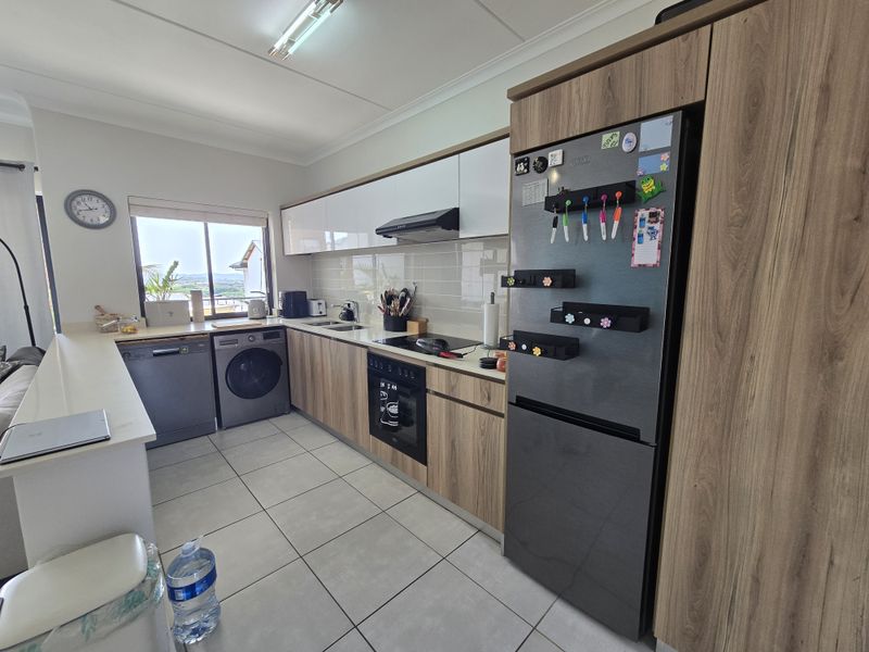 Modern kitchen featuring wood-grain cabinetry, integrated appliances, tiled flooring, and a sleek backsplash, offering a functional and contemporary cooking space.