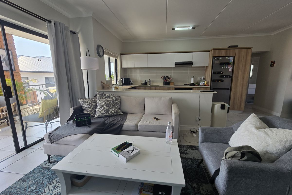 Open-plan living area featuring a modern kitchen with built-in cabinetry and a breakfast counter, seamlessly flowing to a private balcony through sliding glass doors.